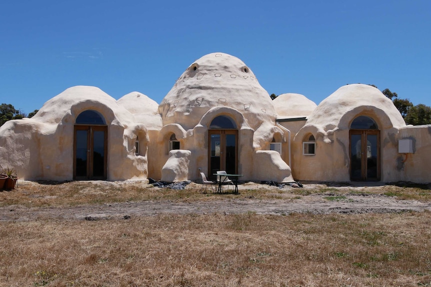 A cream coloured house with three dome roofs in front of a blue sky.