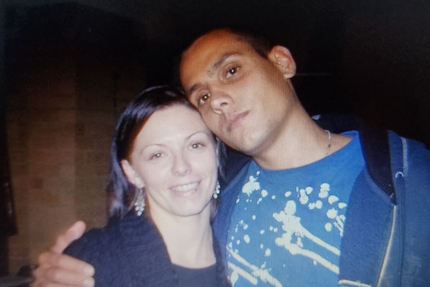 A young Indigenous man in a blue shirt poses with his arm around a young Indigenous woman in a black sweater.
