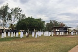 Dozens of white dresses hang on poles in a park.