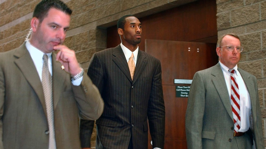 Kobe Bryant in a suit, flanked by security, as he leaves a Colorado court