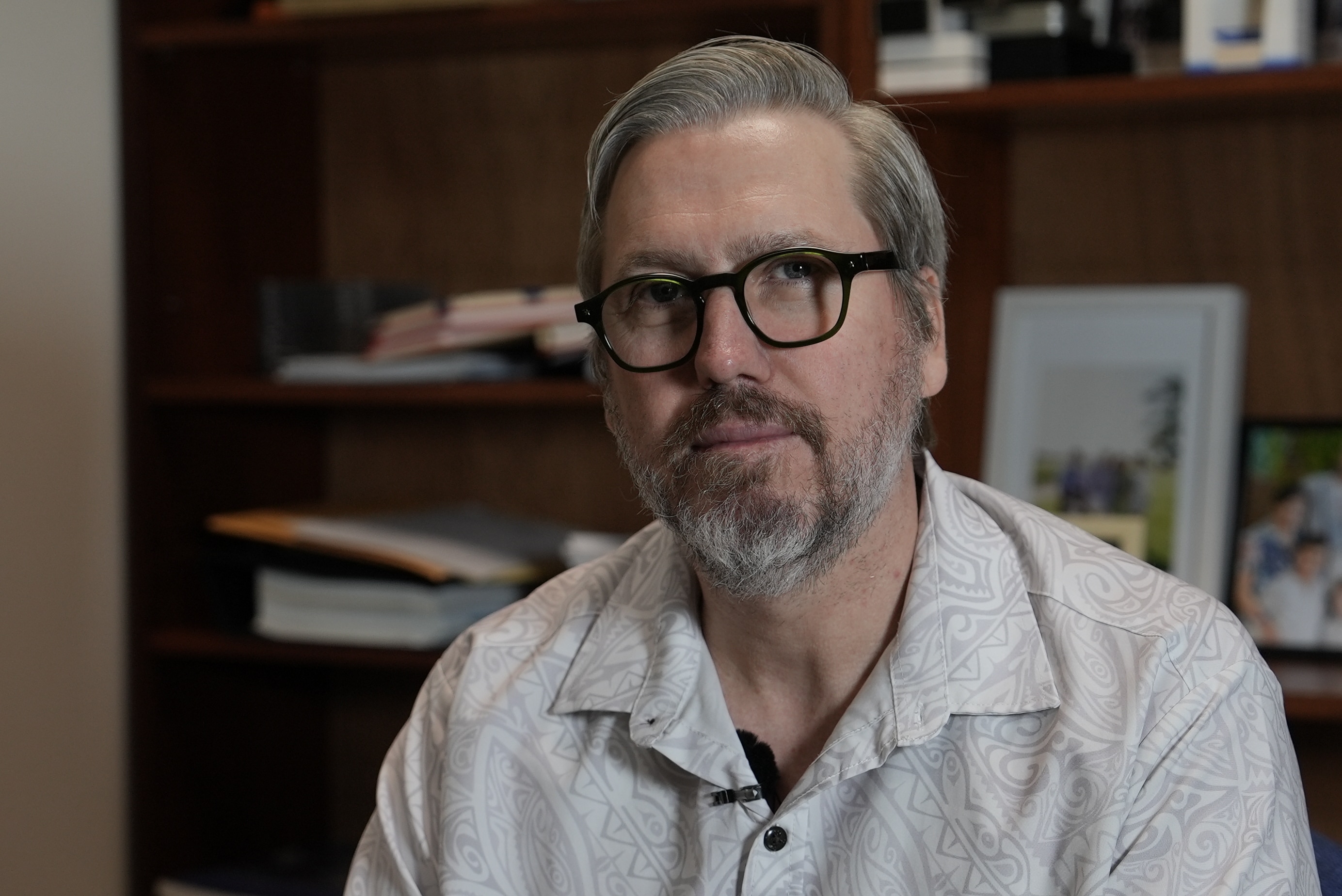 A man in thick-rimmed glasses smiles at the camera.