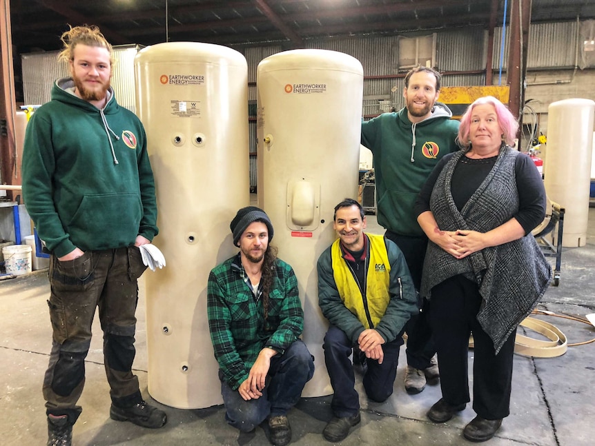 Five workers from the Earthworker Cooperative with two solar hot water systems.