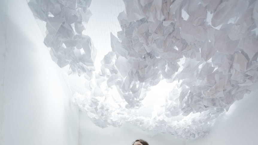 A girl in a white room with scrunched up paper on the ceiling and on the floor