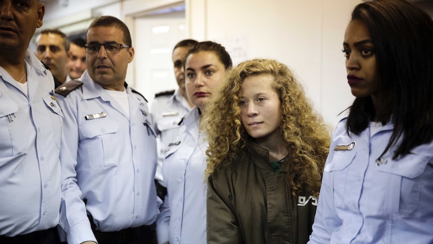 Ahed Tamimi stands in a prison jumpsuit surrounded by guards.