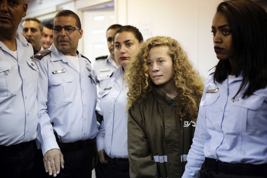 Ahed Tamimi stands in a prison jumpsuit surrounded by guards.