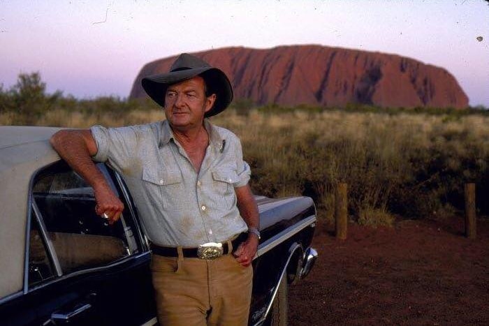 Singer Slim Dusty leans on a car near Uluru