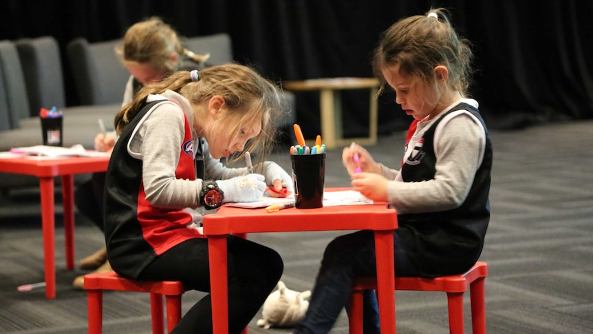 Two children in St Kilda shirts sit at a children's table and draw on paper.