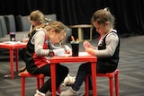 Two children in St Kilda shirts sit at a children's table and draw on paper.