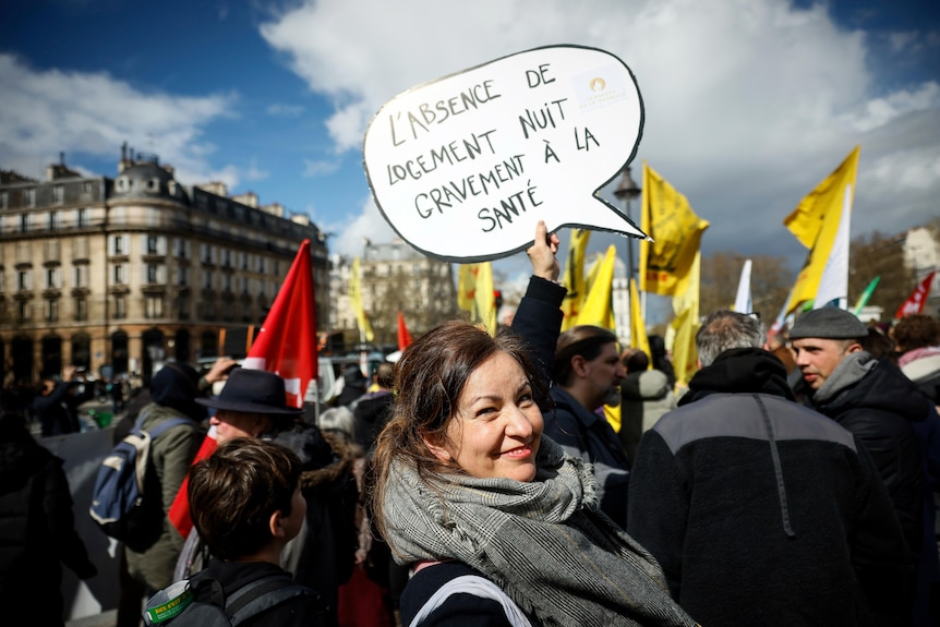 A protester in Paris holds a sign in French that reads: "Lack of Housing Seriously Harms Health".