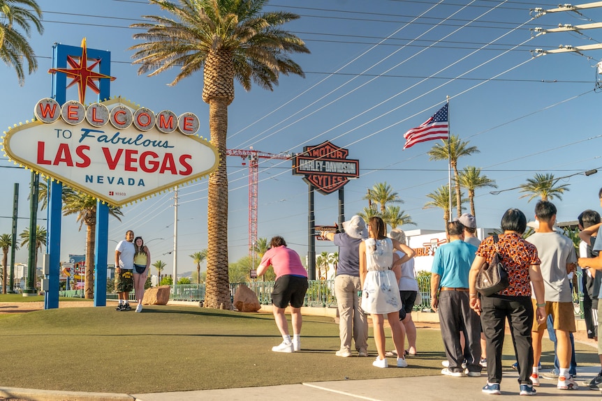A couple stands under a sign that says 'welcome to fabulous Las Vegas' for a photo.