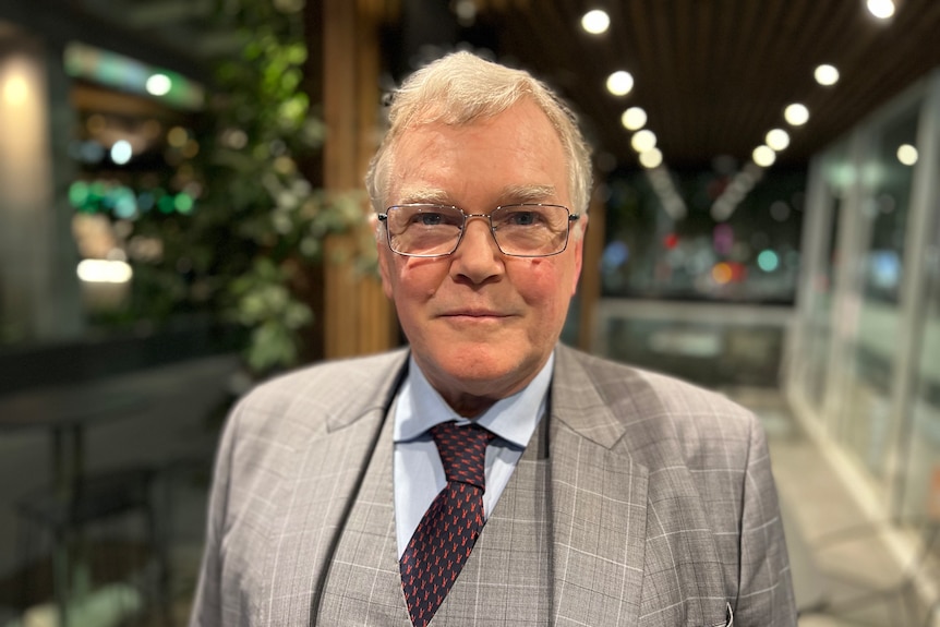 A man wearing a suit and tie and glasses looks into camera