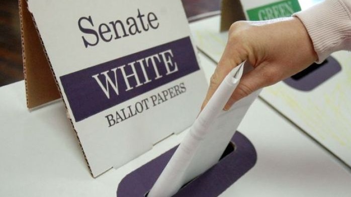 A close-up image of a woman's hand putting a ballot paper into a Senate ballot box.