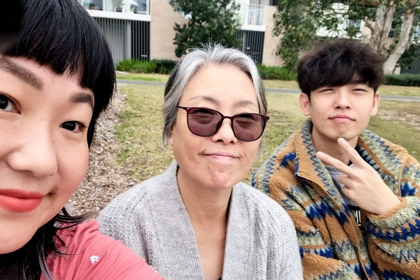 Three people sit in a park and take a selfie