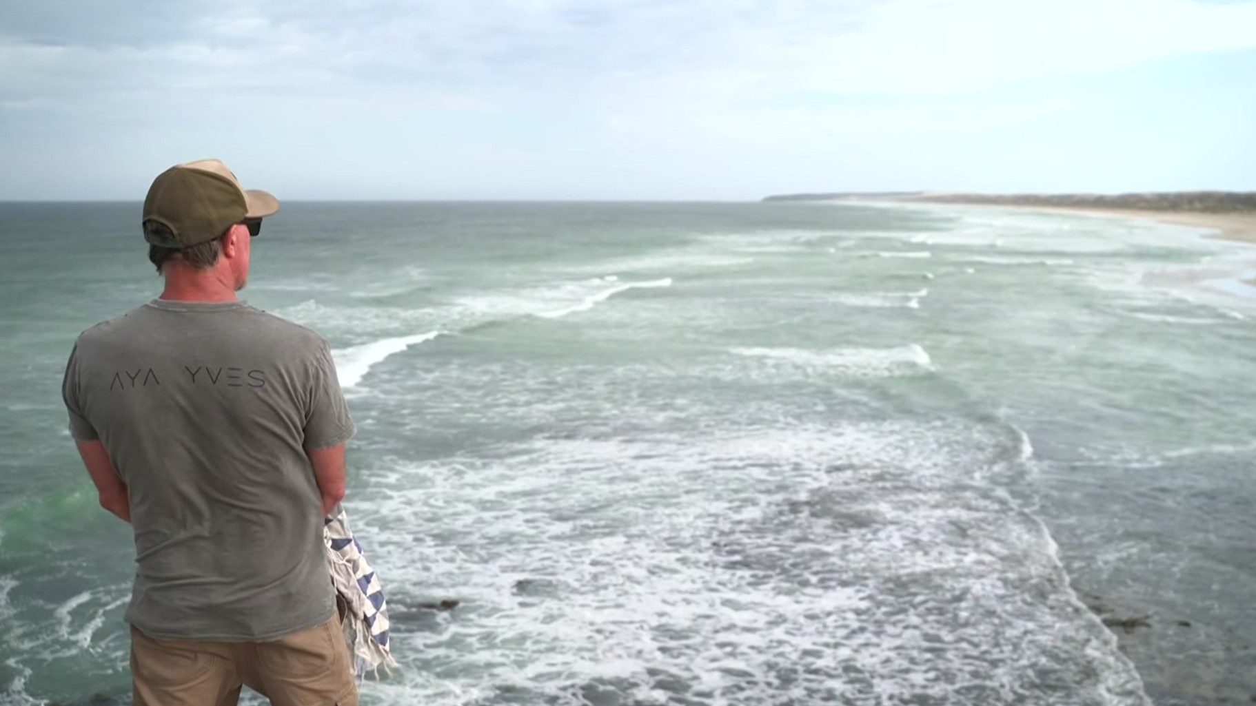 Un hombre aparta la mirada de la cámara hacia el mar cerca de la playa.