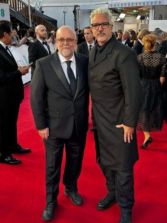 Two men standing on a red carpet.