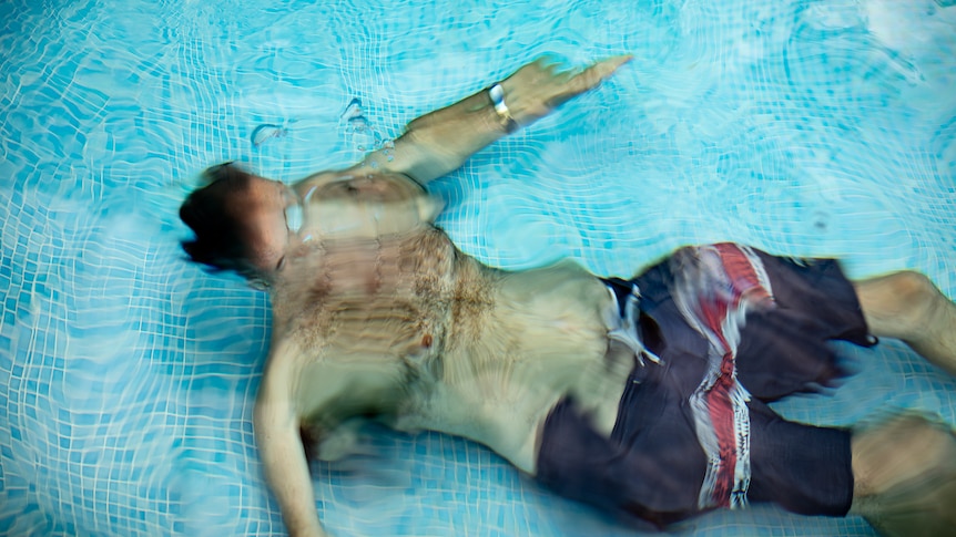A shirtless man sits at the bottom of his pool under water.