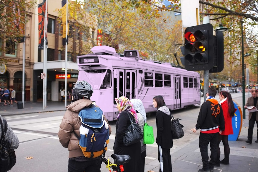 People in Melbourne street spending their time commuting, while a tram travels through.