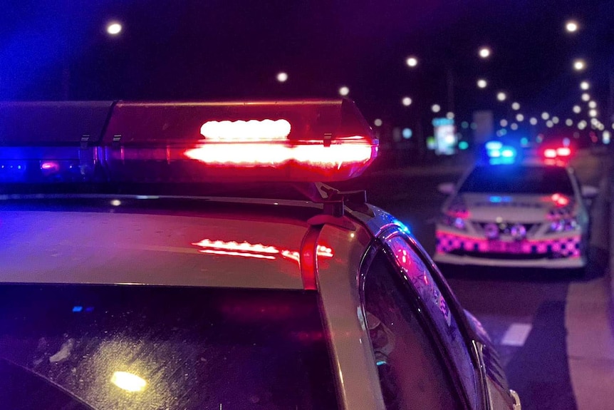 Two police cars on a city street at night, sirens blazing