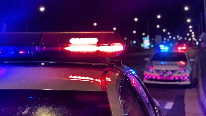 Two police cars on a city street at night, sirens blazing