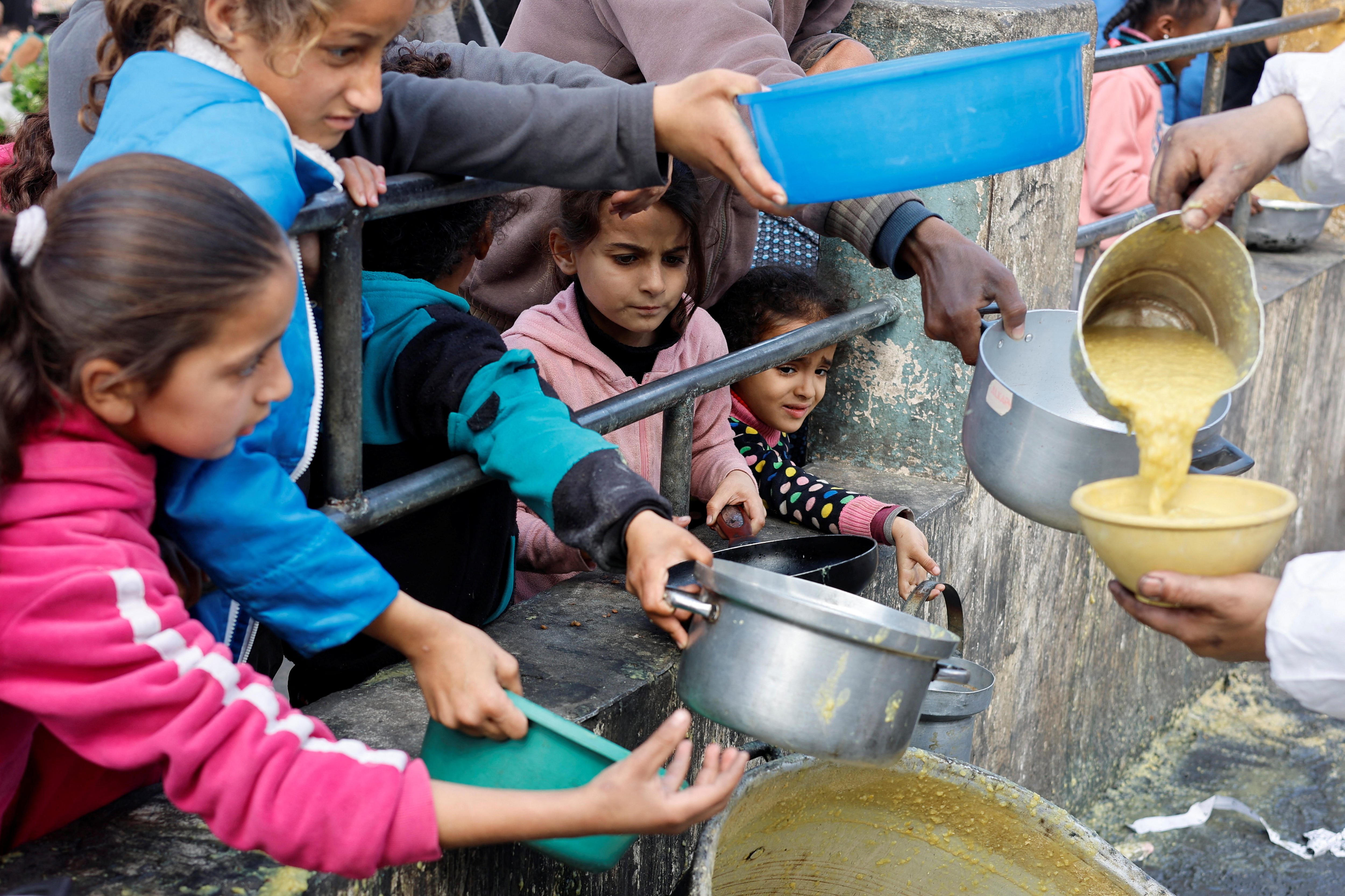 Five little girls hold out bowls while a yellow mixture is pour into one