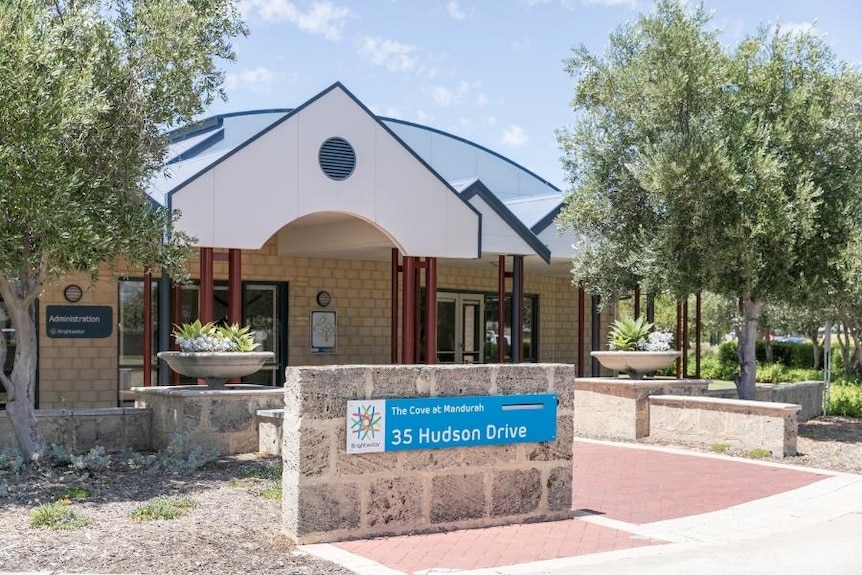 A brick building with a sign indicating that it is a nursing home in a suburban area beneath a sunny sky.