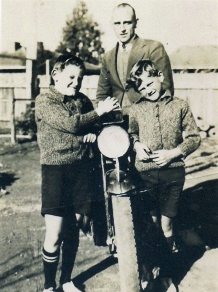 A black and white photograph of a man with two boys, posing with a motorbike.