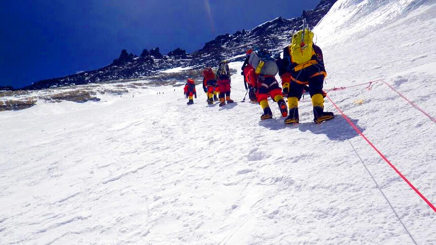 A group of climbers ascend Mount Everest in single file.