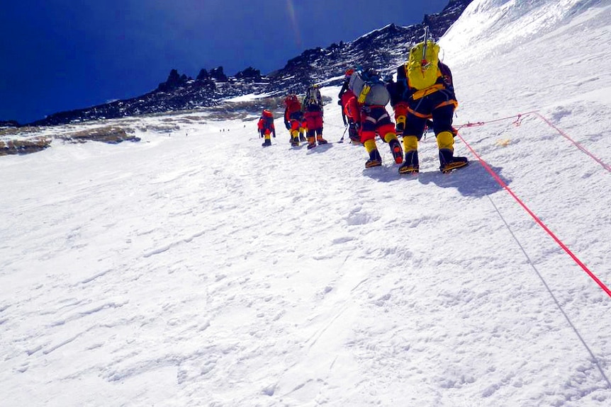 A group of climbers ascend Mount Everest in single file.