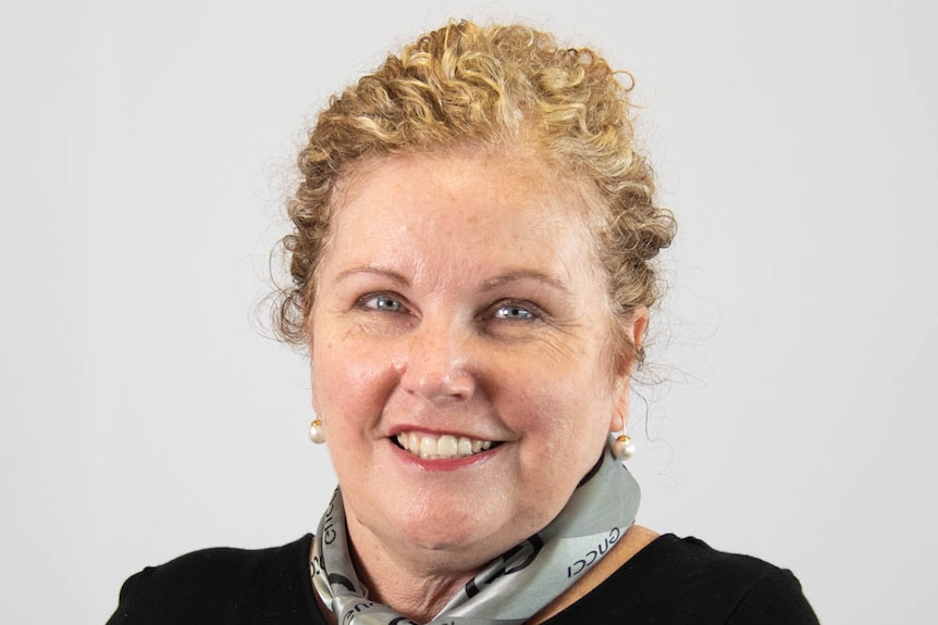 A woman has blond curly hair tied back. She is wearing a black shirt and is smiling.