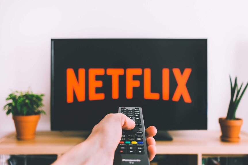 A TV remote pointed at a TV screen with Netflix logo on it