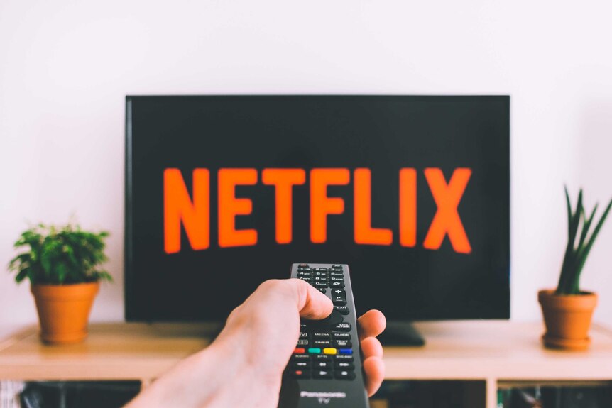 Hand pointing remote at television with 'Netflix' written on the screen.