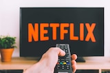 Hand pointing remote at television with 'Netflix' written on the screen.