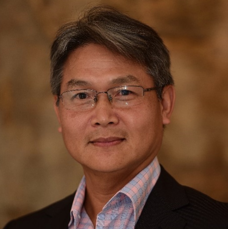 An Asian man with grey hair and wearing glasses.