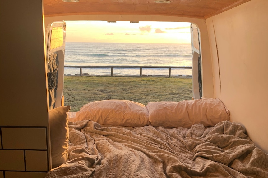 From the inside of the back of a van, the doors open to a water view at sunrise.