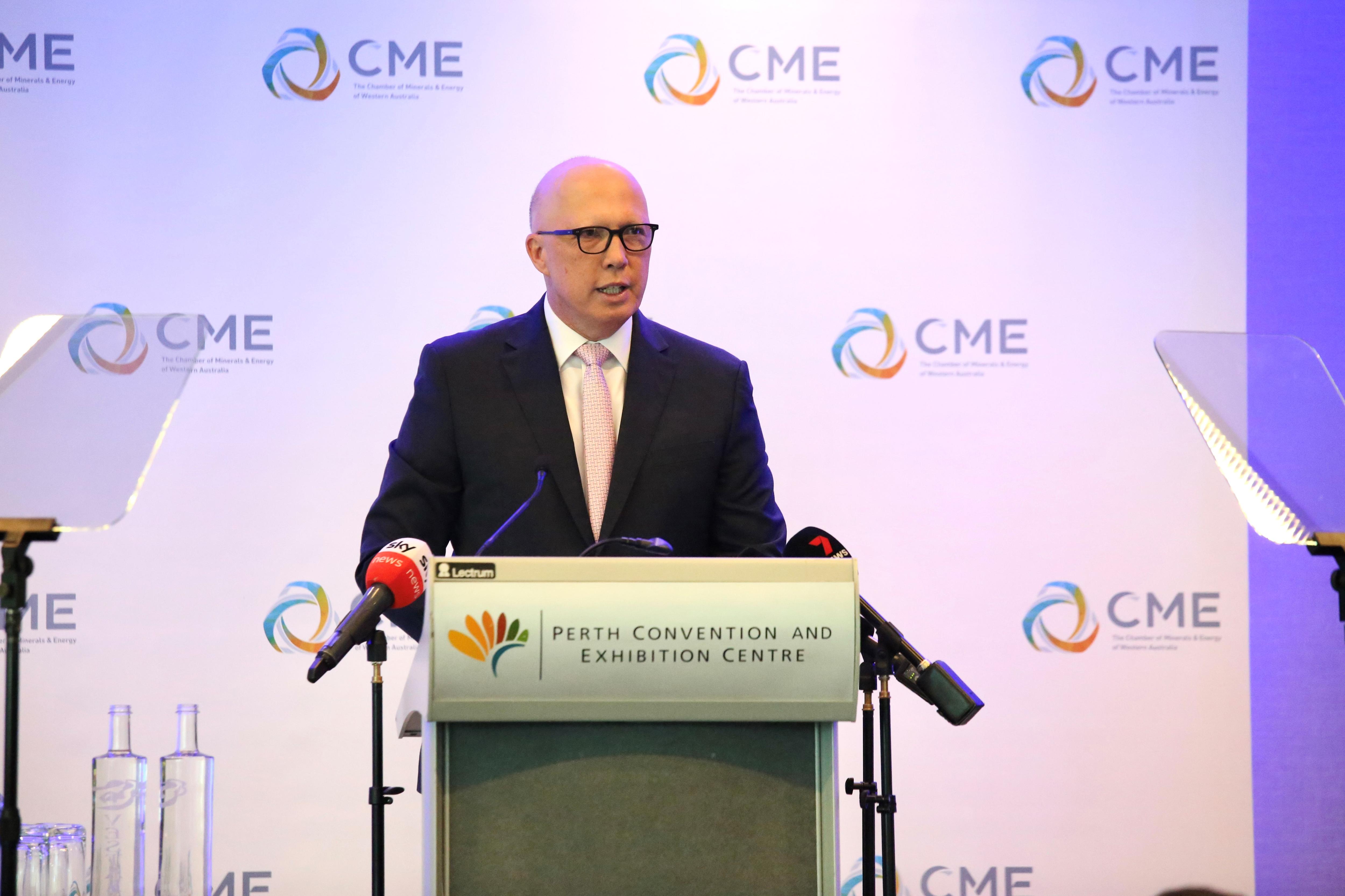 Dutton stands at a lectern speaking, a poster with CME logos behind him.