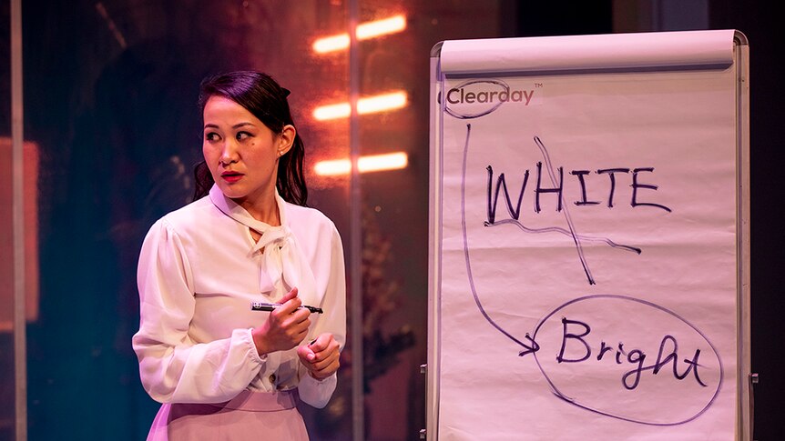 Mayu Iwasaki with marker pen in hand, stands with large post-it easel pad with the word 'white' crossed out and 'bright' circled