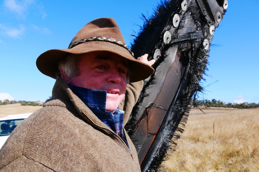 A man stands next to a large object wedged into the ground in a paddock