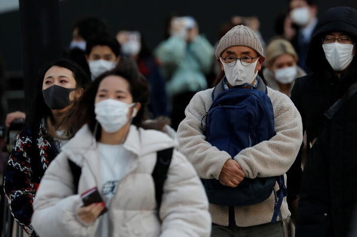 About 10 people are seen walking down a street wearing face masks of a variety of colours in Japan.