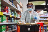Masked woman stacks medicine shelf