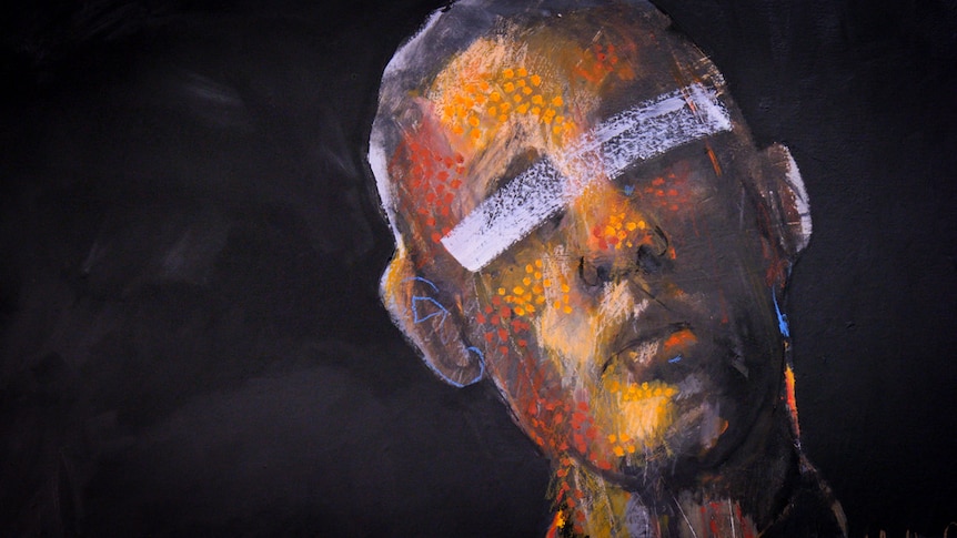 A painting of an Indigenous man's face, with red and yellow dots on his face and a white painted slash across his eyes.