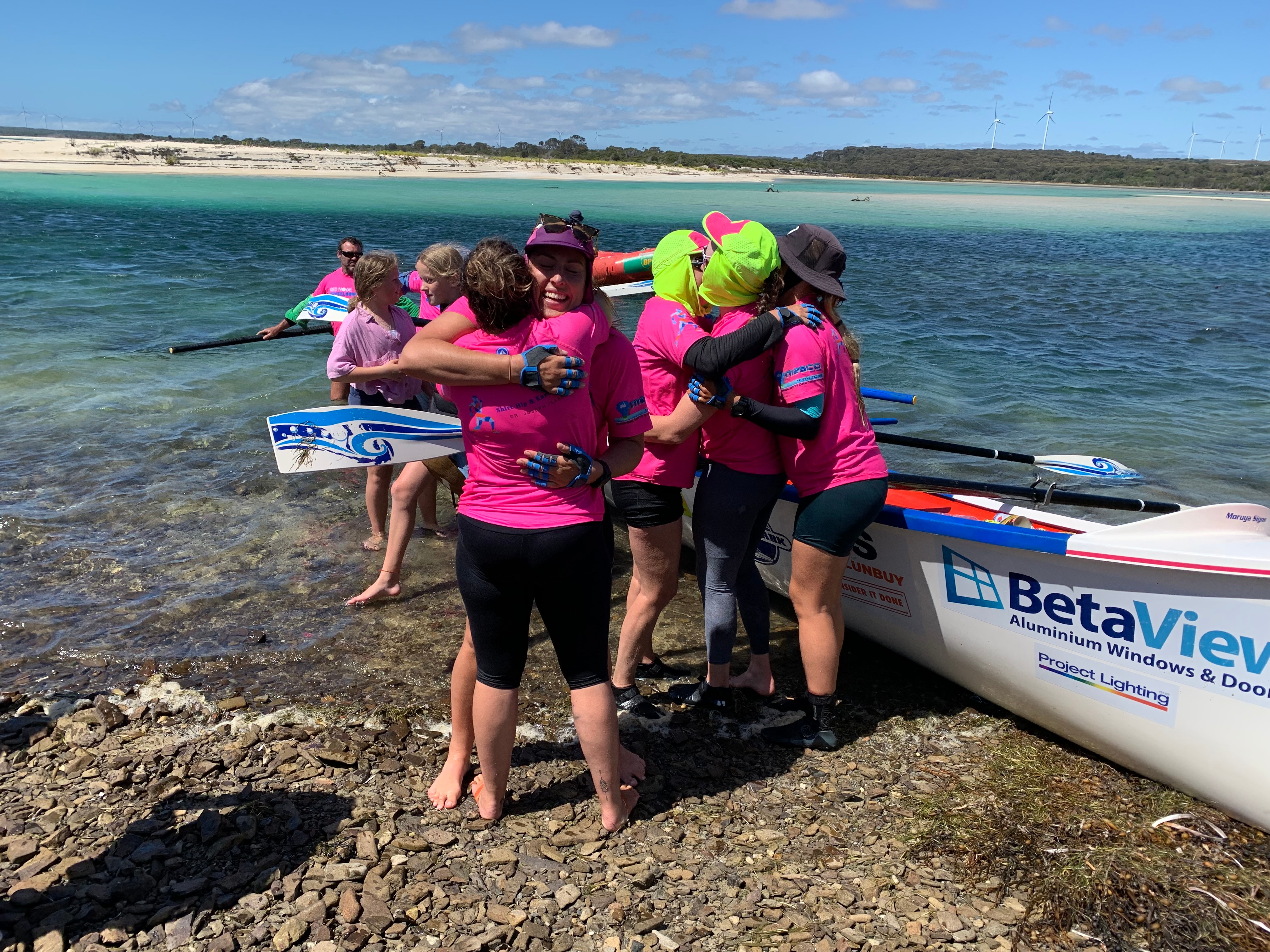 Women wearing pink shirts row a boat into shore