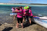 Women wearing pink shirts row a boat into shore