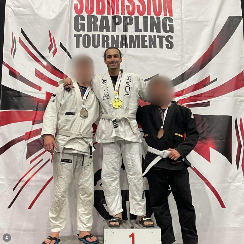 Three men stand on a podium as the top three winners in a Brazilian Jui Jitsu competition. 