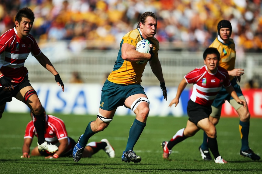 A Wallabies forward runs downfield as Japanese players trail behind him during a Rugby World Cup game.