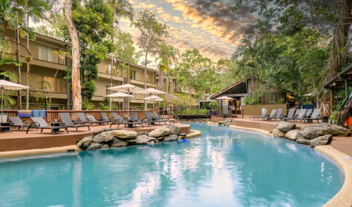 resort pool surrounded by trees and deck chairs