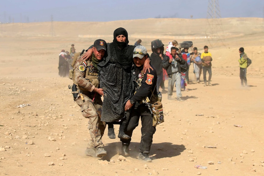 Iraqi security forces help a displaced Iraqi woman flee