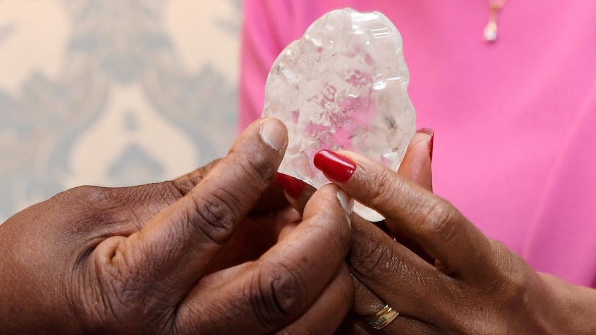 A man and a woman's hand hold a large diamond 