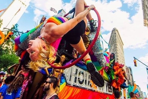 A performer in rainbow costume hangs upside down from a suspended hoop.