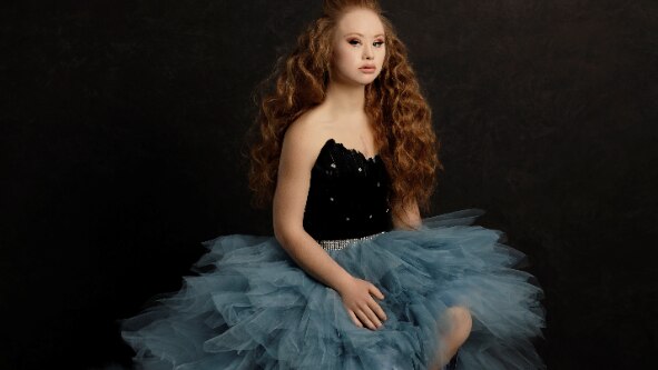 Maddie in a blue tutu and black corset with red hair flowing in waves, background in pitch black.