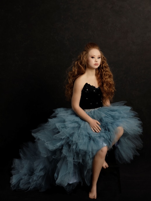 Maddie in a blue tutu and black corset with red hair flowing in waves, background in pitch black.